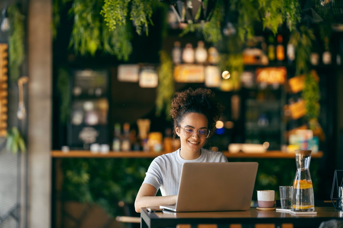 Portrait of happy freelancer sitting in cafe and typing on laptop. A girl is finishing her freelance project.
