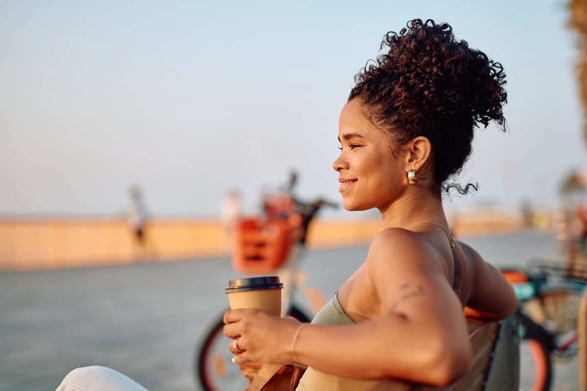 Woman enjoying a coffee outdoors on a sunny day, relaxed and smiling