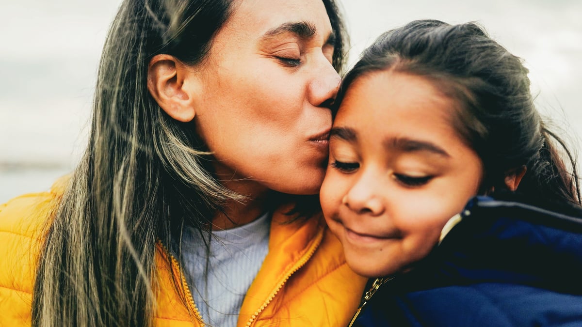 Happy latin mother hugging her daughter outdoors, family bonding moment