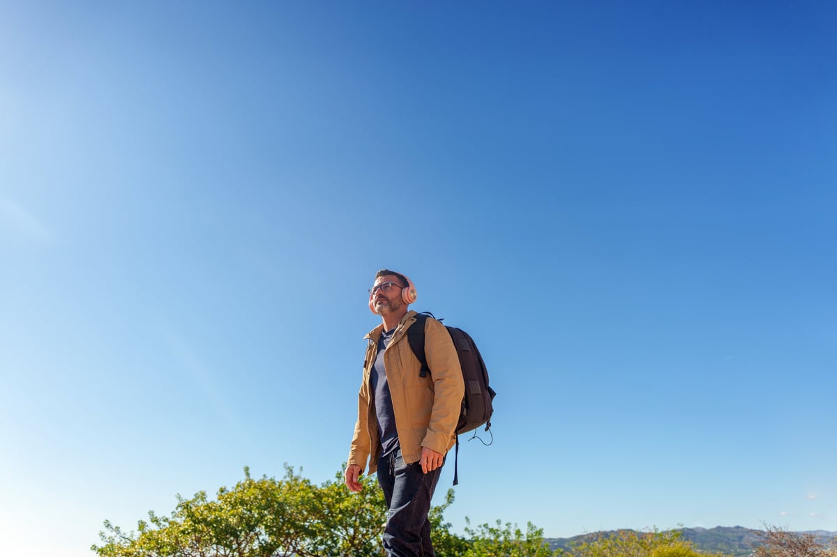 Mid adult man with a backpack and headphones hiking and traveling under a clear blue sky