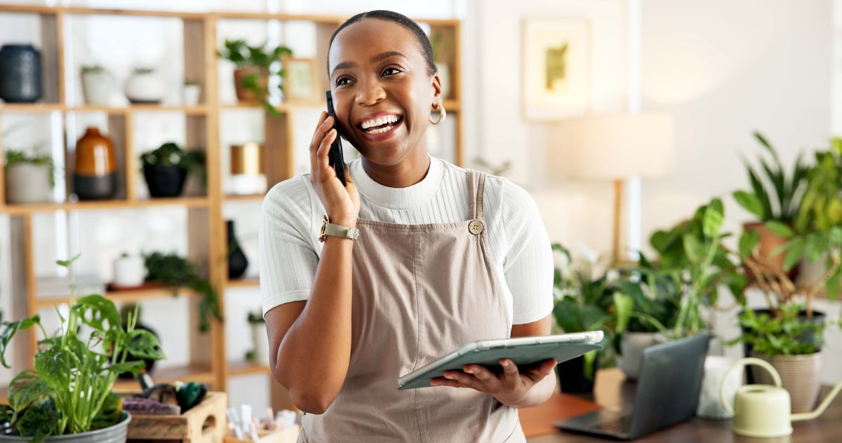 Small business owner on a phone call with a tablet in her shop, confirming an online order