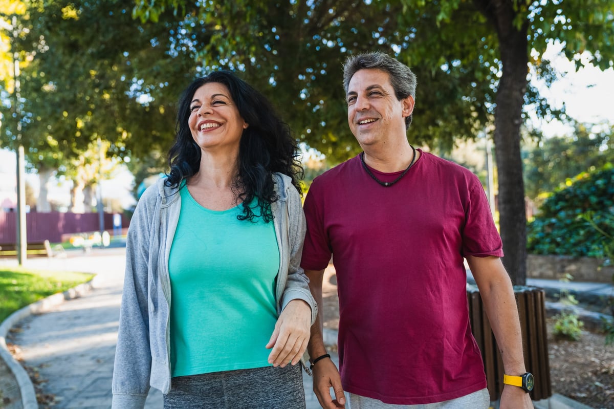 Cheerful middle aged couple enjoying a leisurely walk in a sunny park, embracing active lifestyle and wellness outdoors